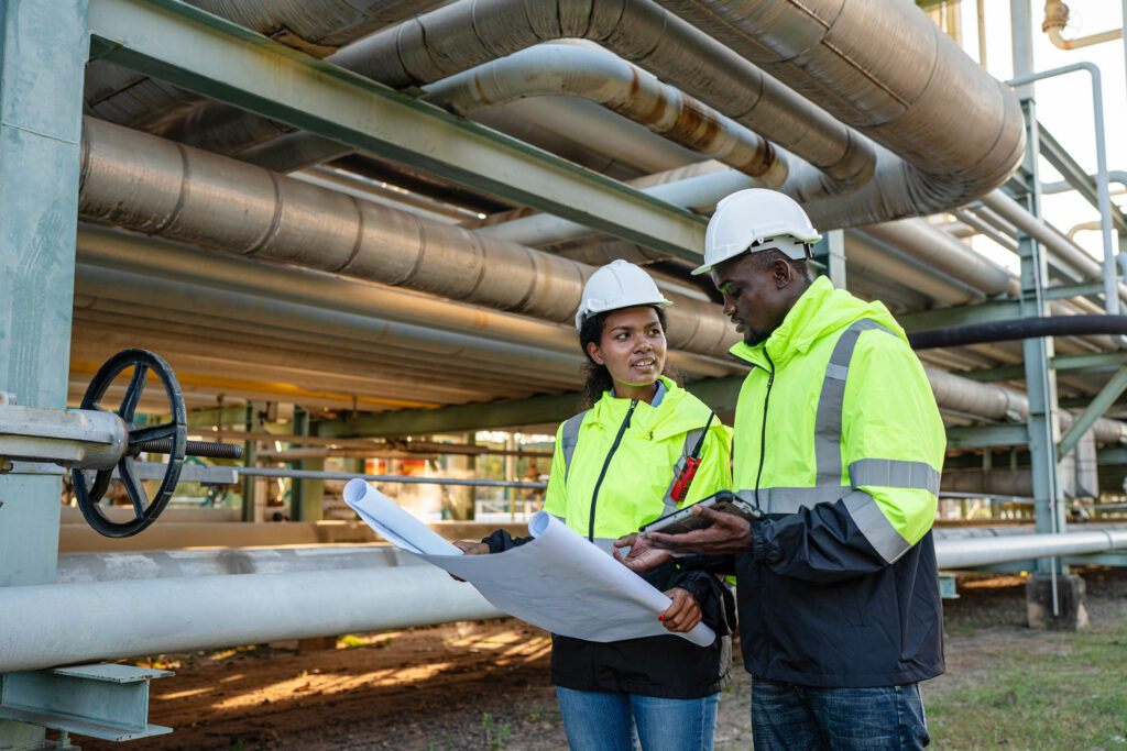 Young mechanical engineer holding blueprint drawing to checking and inspection gas pipeline system new construction project of industrial.